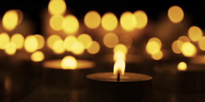 A burning candle with further candle light in the background.