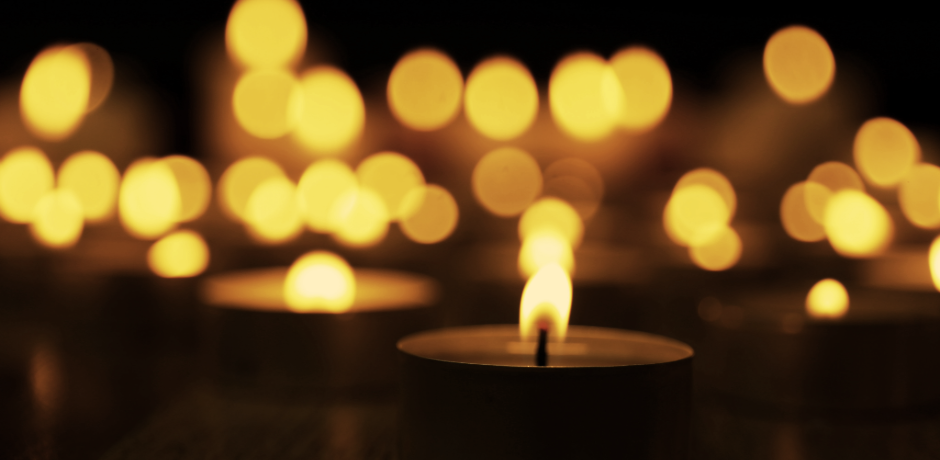 A burning candle with further candle light in the background.