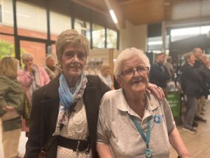 Two women standing together, with a crowd behind them in the foyer at Causeway Hospital.