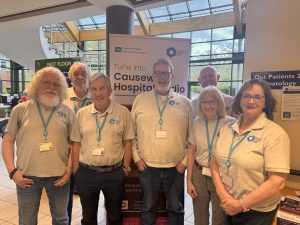 Hospital radio volunteers stand in the foyer cafe area, with a pop-up banner behind them.