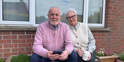 An older man and woman sitting outside a red brick house.