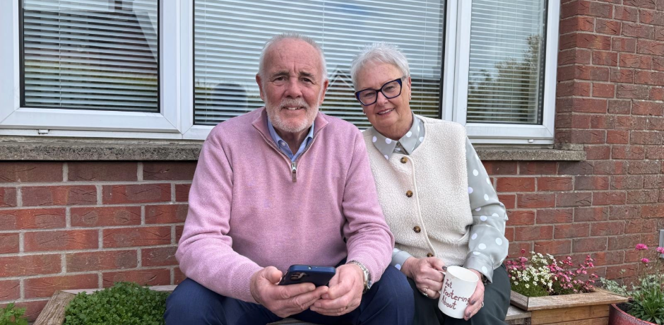 An older man and woman sitting outside a red brick house.