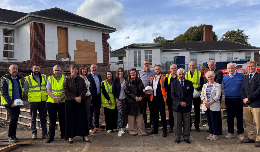 A large group of people, some wearing high viz and holding hard hats, standing at the site of building works at Robinson Memorial Hospital.