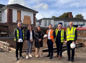 A group of people, some wearing high viz and holding hard hats, standing at the site of building works at Robinson Memorial Hospital.
