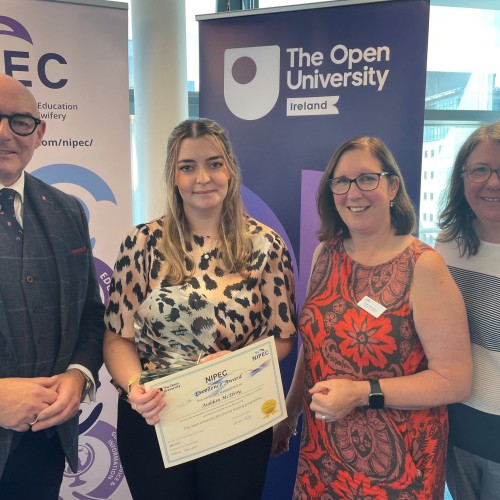 Northern Trust nurse Aiobhin McElroy pictured with her highly commended award, along with (L-R), John D’Arcy, National Director OU Ireland, Cathy McCusker from NIPEC and Donna Gallagher, Open University Professional Lead for School of Health and Wellbeing & Social Care. Aiobhin McElroy holding her highly commended award, along with John D’Arcy, National Director OU Ireland, Cathy McCusker from NIPEC and Donna Gallagher, Open University Professional Lead for School of Health and Wellbeing & Social Care. standing in front of pop-up banners.