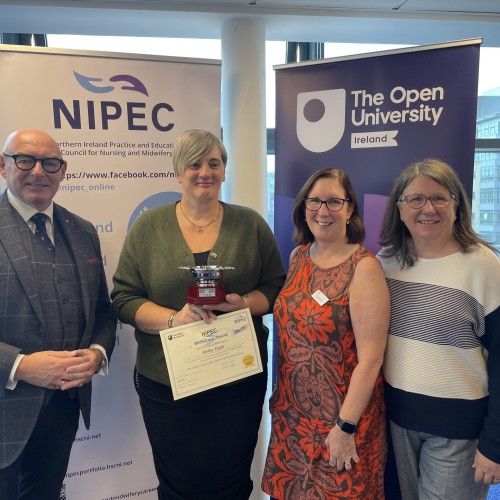 Northern Trust nurse Shelley Taylor pictured with her Student Excellence award, along with (L-R), John D’Arcy, National Director OU Ireland, Cathy McCusker from NIPEC and Donna Gallagher, from Open University Professional Lead for School of Health and Wellbeing & Social Care. Shelley Taylor holds her Student Excellence award, along with John D’Arcy, National Director OU Ireland, Cathy McCusker from NIPEC and Donna Gallagher, from Open University Professional Lead for School of Health and Wellbeing & Social Care, with pop-up banners behind.