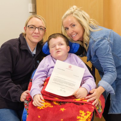 Anna Cahoon pictured with Catherine Whiteford and Kellie Ritchie from Larne Adult Centre. Anna Cahoon holds her letter from Buckingham Palace with two members of staff either side of her,